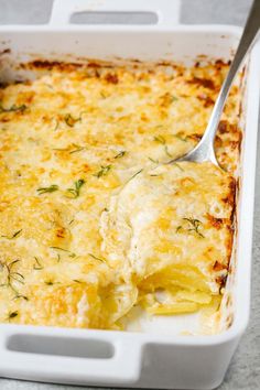 a white casserole dish filled with cheese and herbs, with a spoon in it