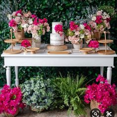 a white table topped with lots of pink flowers and greenery next to a green wall