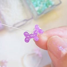 a person is holding a tiny purple flower on a string with some beads in the background