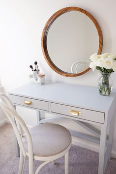 a white desk with a mirror and flowers on it in front of a chair next to the table