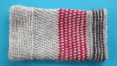 a close up of a knitted object on a blue surface with red and gray stripes