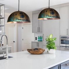 two lights hanging over a kitchen island with a bowl on the counter and potted plant next to it