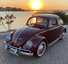 an old car is parked on the side of the road near the water at sunset