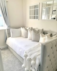 a white couch sitting in front of a window with pillows on it's back