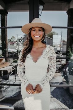 a woman wearing a white wedding dress and cowboy hat standing in front of a window