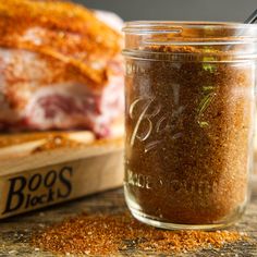 a glass jar filled with spices next to a wooden cutting board and meat in the background