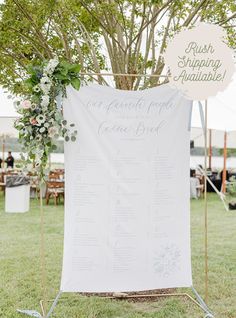 a sign that is on top of a stand in the grass with flowers and greenery