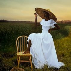 a woman in a white dress and straw hat sitting on a chair