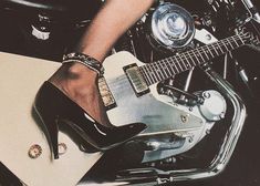 a woman in high heels sitting on top of a motorcycle with a guitar next to her