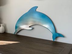 a metal dolphin sculpture sitting on top of a wooden table next to a white vase