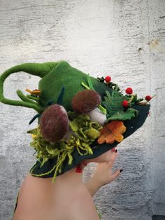 a woman's hand holding a green hat with flowers and leaves on it,