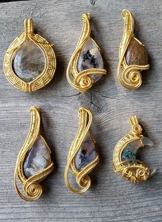 four different pendants are sitting on a wooden surface, one has a stone and the other is wire wrapped around it