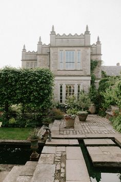 an outdoor patio with potted plants and water in front of a large stone building