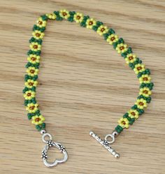 a green and yellow beaded bracelet on a wooden table with a silver heart charm