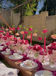 a long table is set with pink flowers and candles in vases, plates and napkins