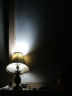 a lamp on a table next to a window in a room with dark walls and flooring