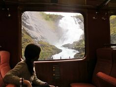 a woman sitting on a train looking out the window at a waterfall in the distance