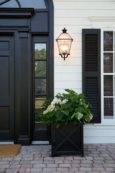 a black door with shutters and a planter on the front porch next to it