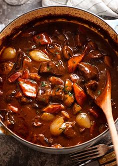 a pot filled with stew and potatoes on top of a table next to a wooden spoon