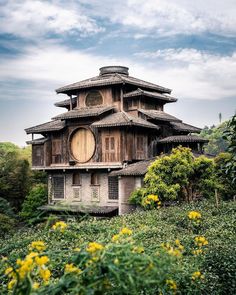 an old building in the middle of a field with yellow flowers and trees around it