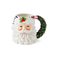 a ceramic mug with a santa claus face and holly wreath on the handle, sitting in front of a white background