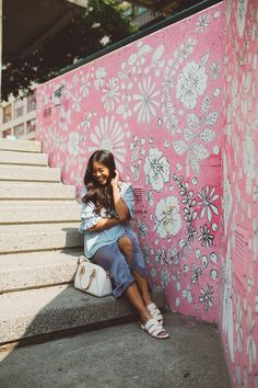 a woman sitting on the steps next to a pink wall with flowers painted on it