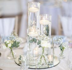 candles and flowers in glass vases on a white table cloth with silverware, plates and napkins