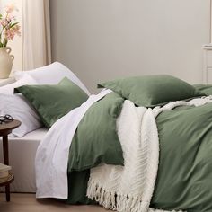 an unmade bed with green and white sheets, pillows and blankets on top of it