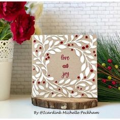 a card with the words love and joy on it sitting next to some red flowers