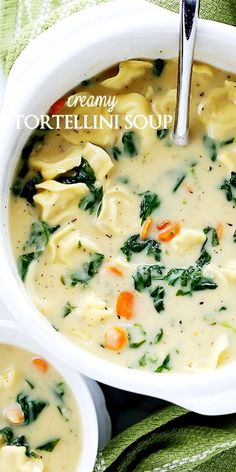 two white bowls filled with tortellini soup on top of a green cloth next to silver spoons