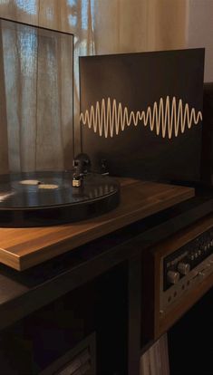 a record player sitting on top of a wooden table next to a window with curtains