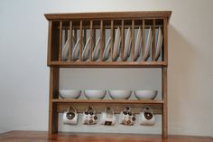 a wooden shelf filled with white dishes and cups on top of each other, next to a wall mounted dish rack