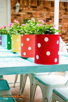 three colorful flower pots sitting on top of a blue table with white polka dot chairs