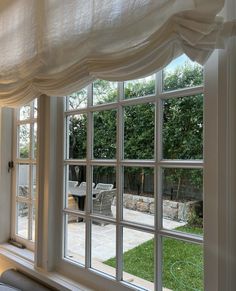 an open window with white curtains on the outside and patio in the back yard behind it