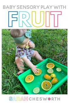 a baby sitting in the grass eating fruit from a green tray with text overlay