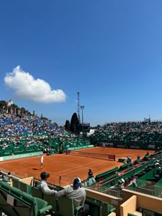 two people sitting in chairs watching a tennis match on a clay court with green seats