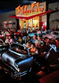 an old car is parked in front of a restaurant with many people sitting around it