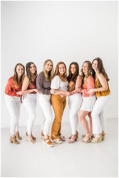 a group of women standing next to each other in front of a white wall with their arms around each other