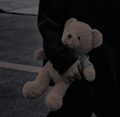 a person holding a teddy bear in their hand on the street at night with other people nearby