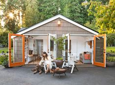 a woman sitting on a chair in front of a shed with orange doors and windows