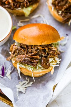 two pulled pork sandwiches with cole slaw and ranch dressing on the side, sitting on wax paper