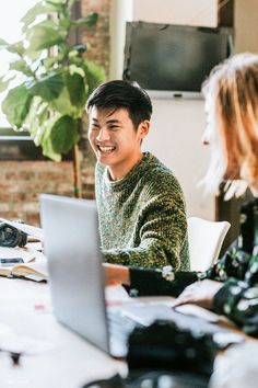 two people sitting at a table with laptops in front of them, one smiling and the other laughing