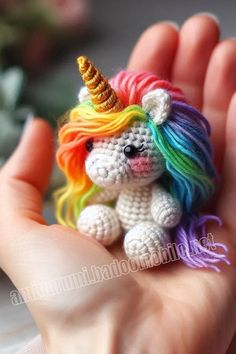 a tiny crocheted unicorn is sitting in someone's hand with it's head turned to the side