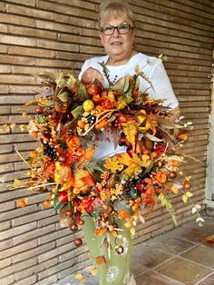 an older woman holding a wreath with autumn decorations