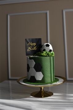 a soccer themed birthday cake on a gold pedestal with a black and white ball sitting on top