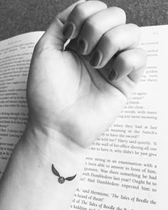 a woman's hand holding an open book with a small tattoo on the wrist