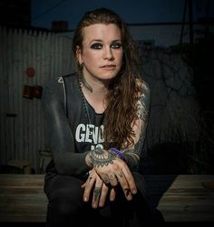 a woman with tattoos and piercings sitting on a bench in front of a fence