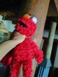 a hand holding a red stuffed animal on top of a wooden pole