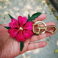 a pink flower with green leaves on it being held by a person's hand