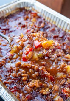 a spoon with some food in it on top of a tin foil pan filled with sauce